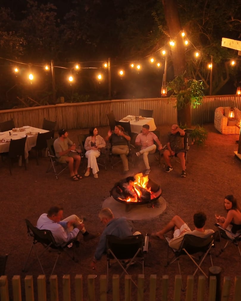 Guests gathered around the fire bowl in the boma at night, under strings of festoon lights