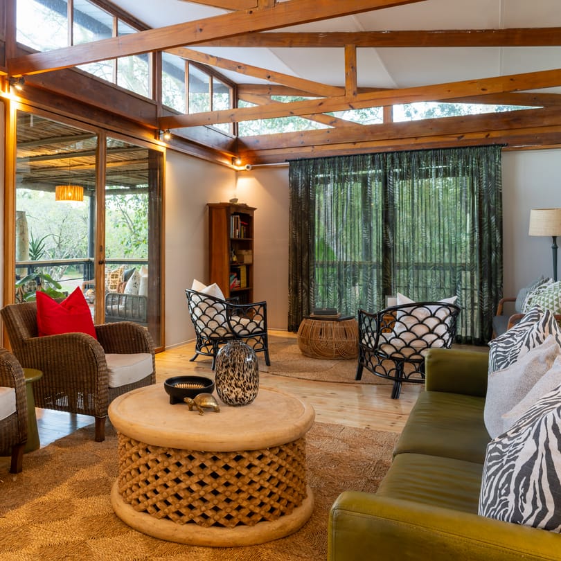 The lounge of the main lodge, rattan armchairs with red cushions round a carved table