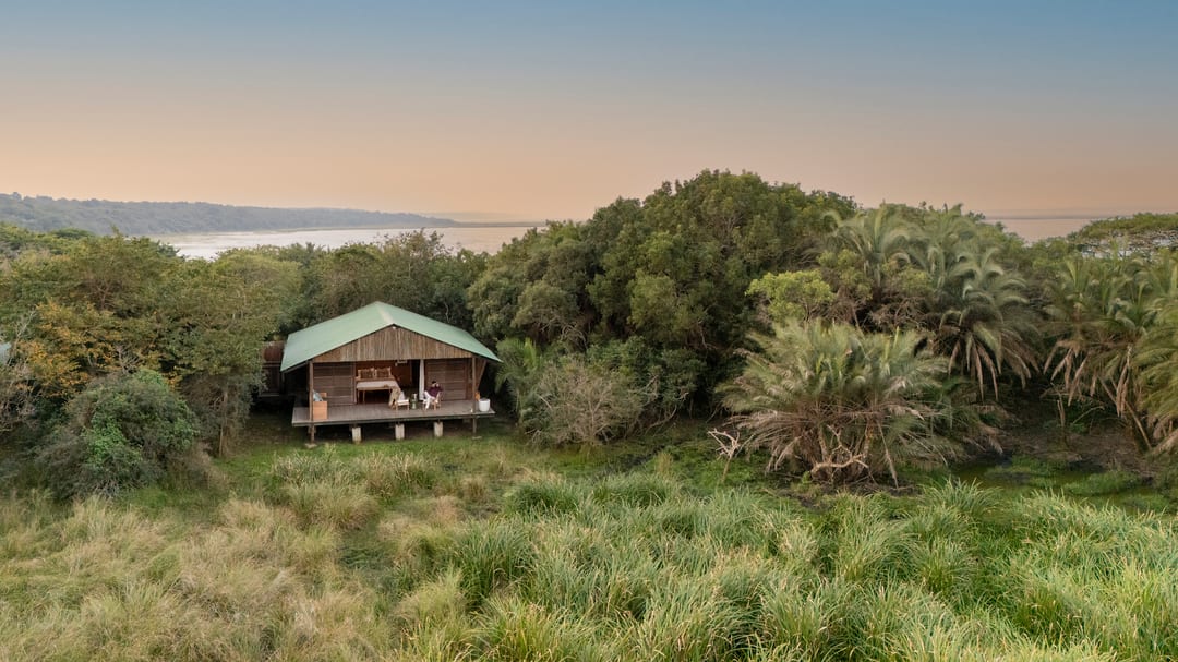 A suite on its raised deck among coastal forest at dusk, the lake and a pastel sky beyond.