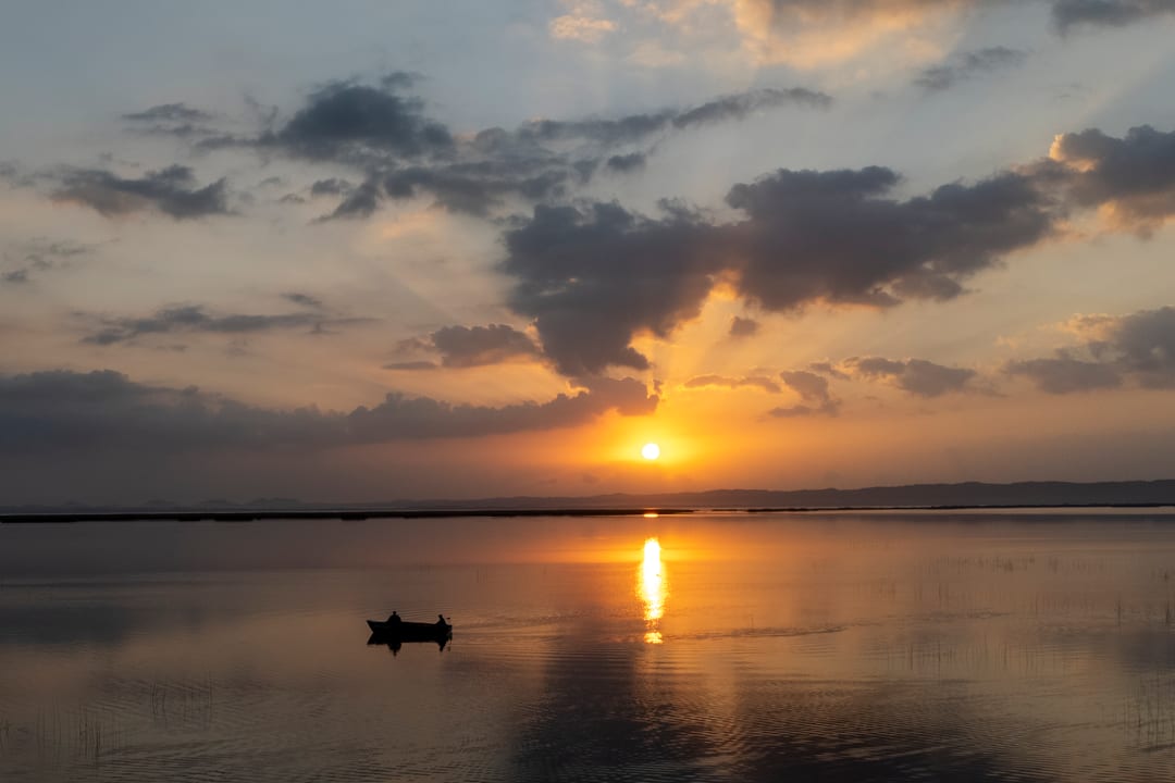 A small eco-boat with two people aboard on still water as the sun breaks through cloud.