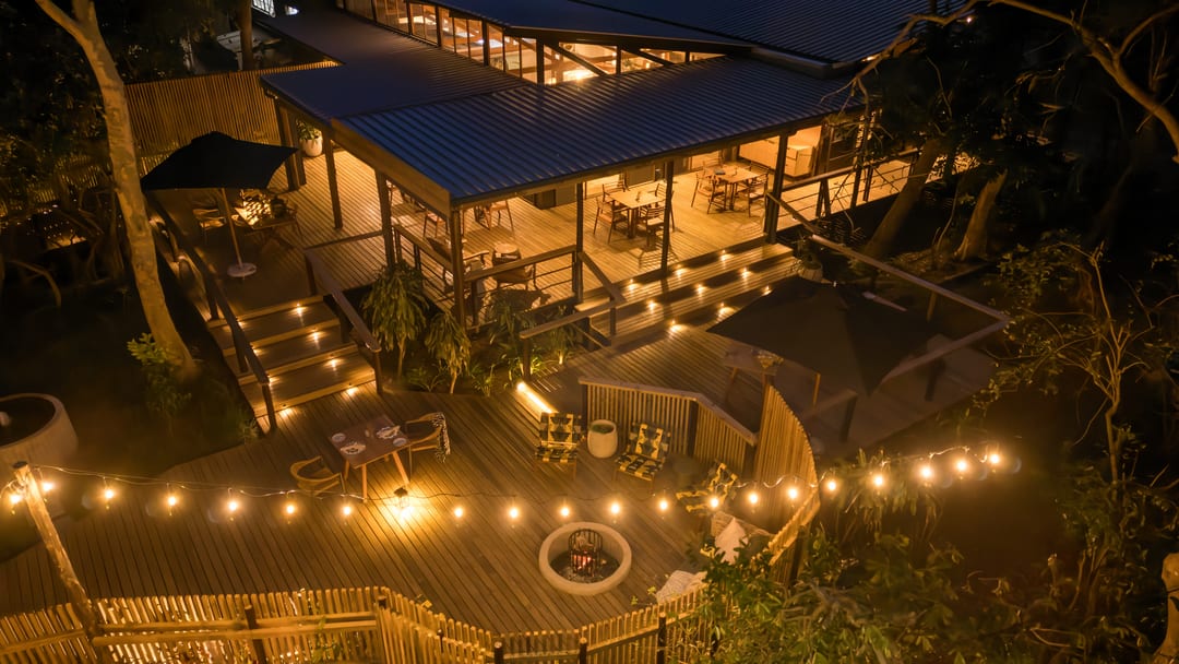 The main lodge and its extended deck from the air at night, lit by deck lights and string lights.