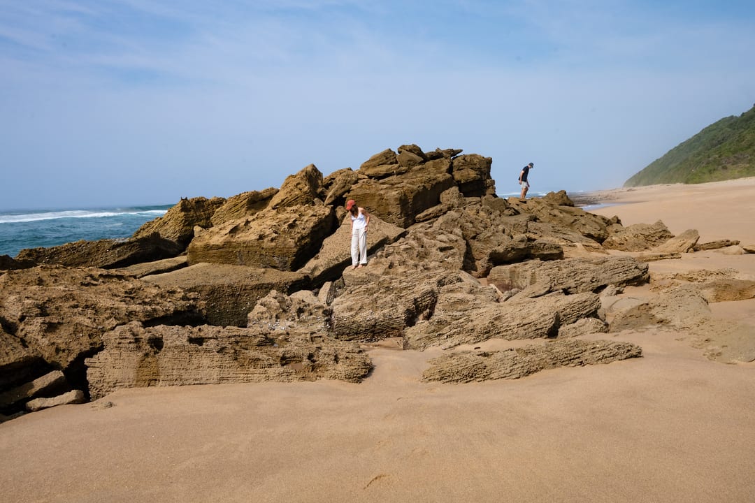 A weathered rock outcrop on the beach with two guests small on the rocks
