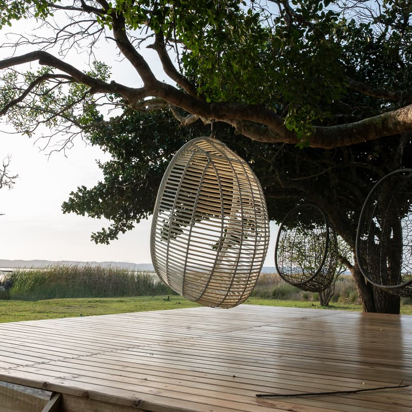 Hanging egg chairs under a big tree on the deck at the water’s edge, the lake beyond