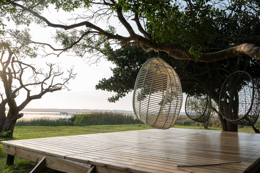 Hanging egg chairs under a large tree on the waterside deck in soft morning haze