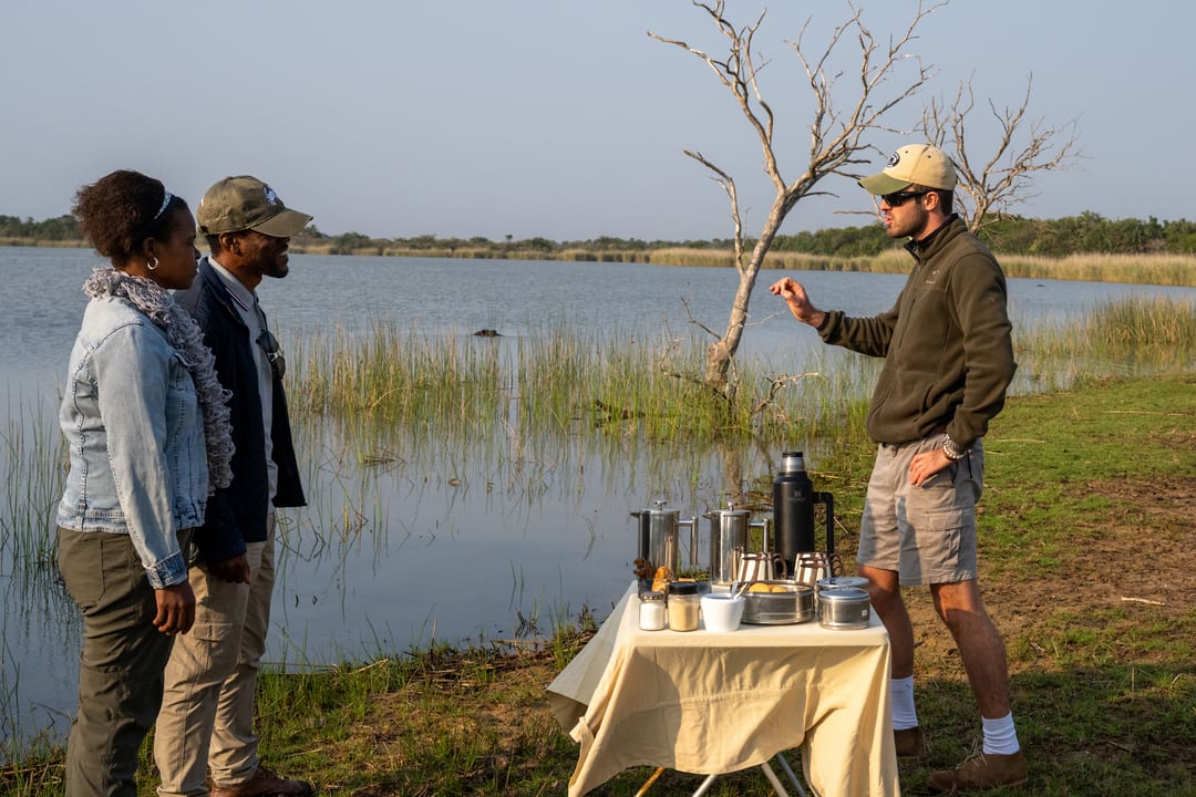 The guide talks with two guests across a coffee table on the lakeshore