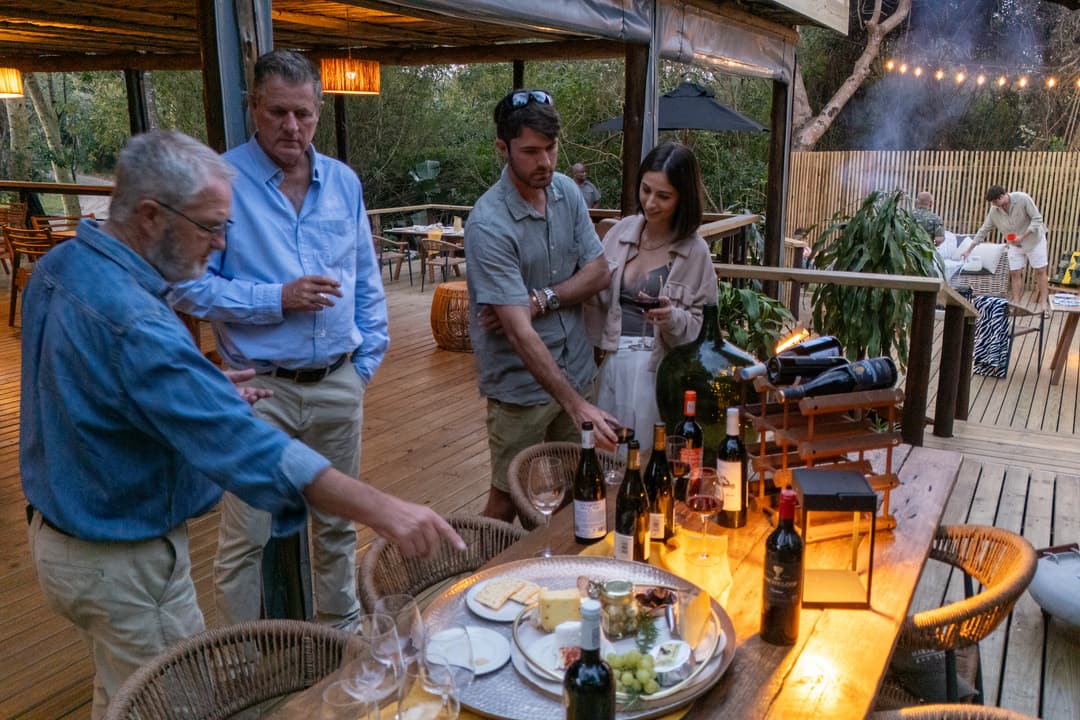 Guests gather round wine and a cheese platter by lantern light on the deck at dusk