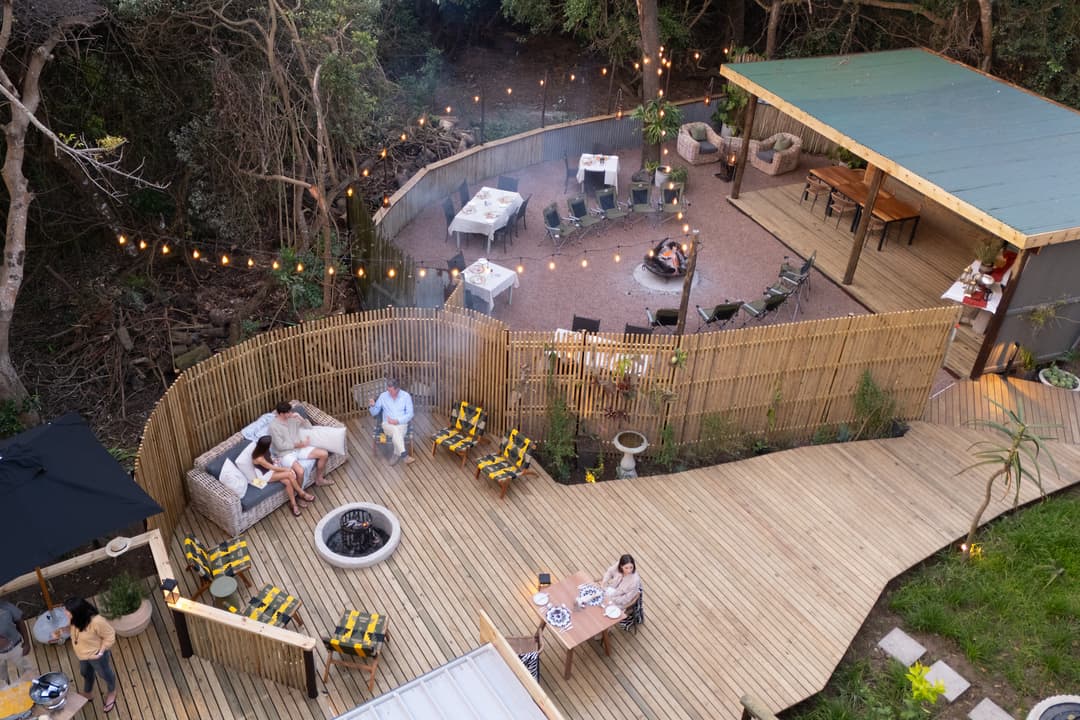 The deck boma and main boma from above at dusk, guests settling on sofas by the fire