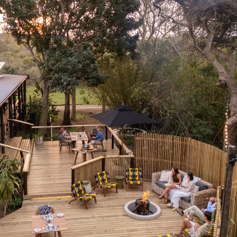 The extended deck of the main lodge at dusk, guests gathered round the fire on the deck