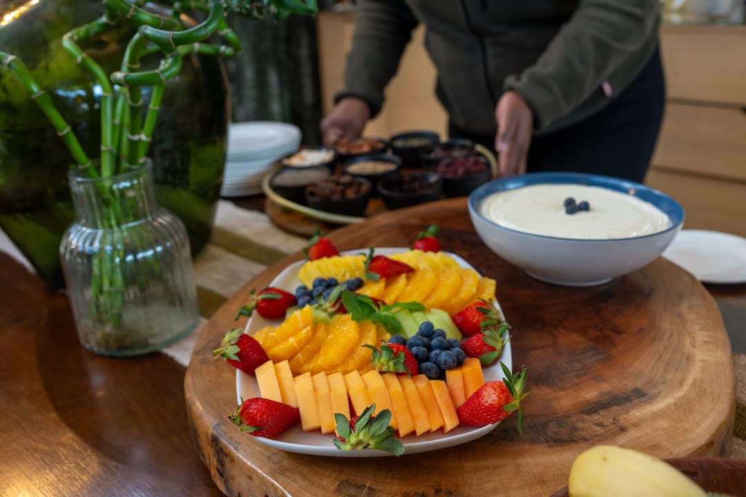 A breakfast platter of melon, orange, strawberries and blueberries beside a bowl of yoghurt