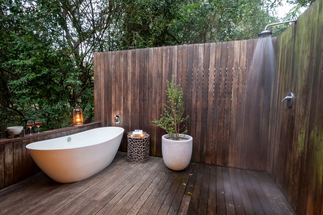 An outdoor bath and rain shower on a private timber deck at dusk, forest beyond