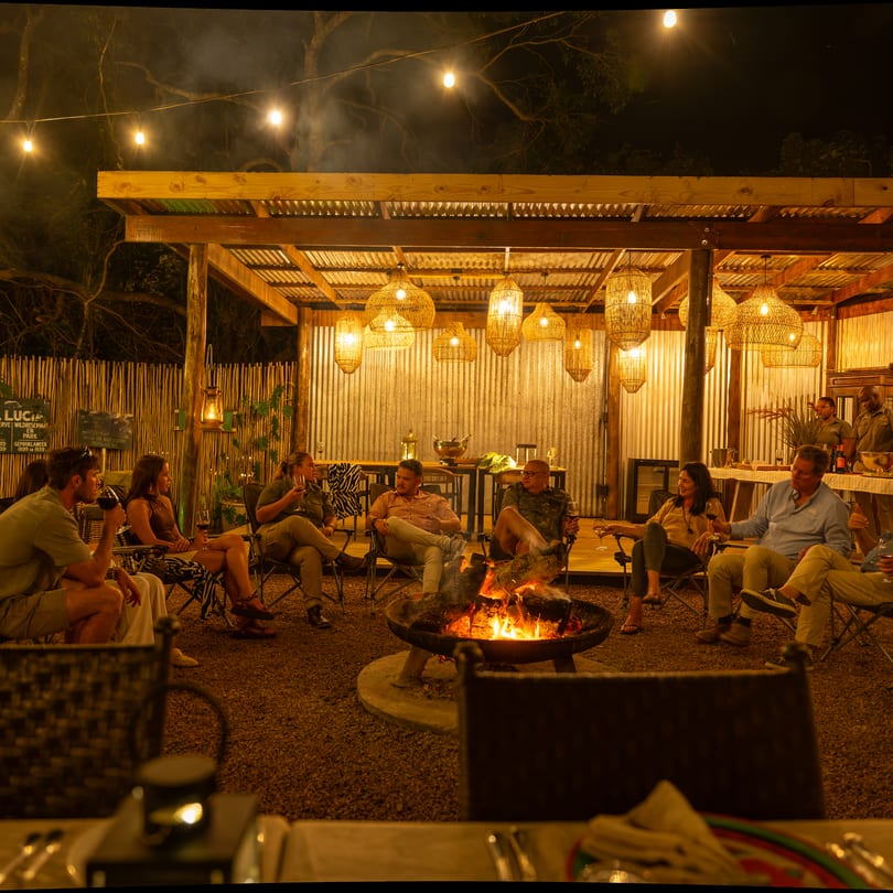 Dinner tables laid in the main boma at night, guests round the fire and lanterns lit in the pavilion