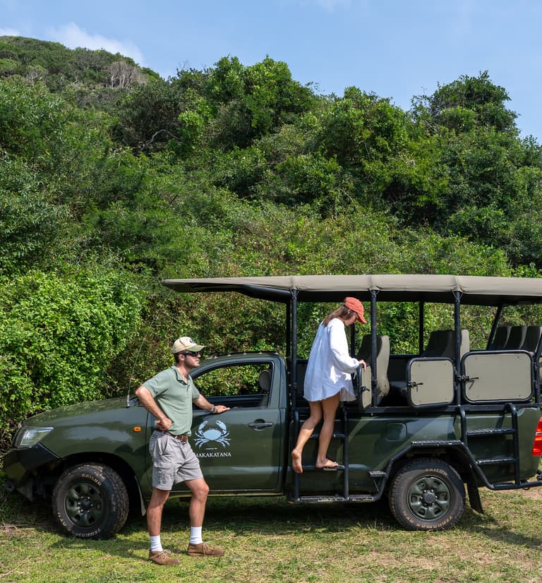 Our guide leans on the open game-drive vehicle as guests climb aboard at the beach access.