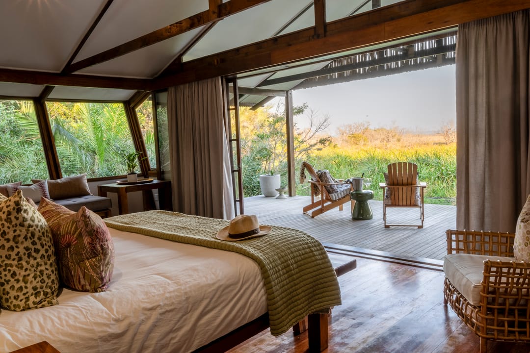 A suite bedroom at golden hour, doors open onto a timber deck and wetland grasses