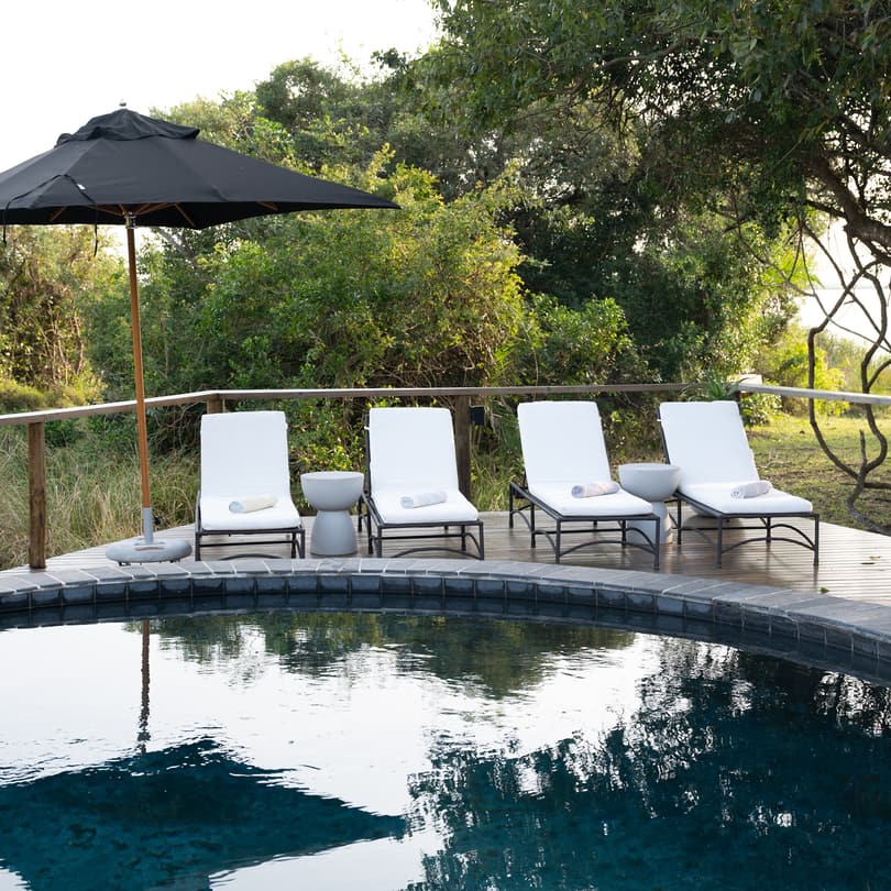 The round pool on the pool deck, white loungers under a black umbrella, the lake through the trees