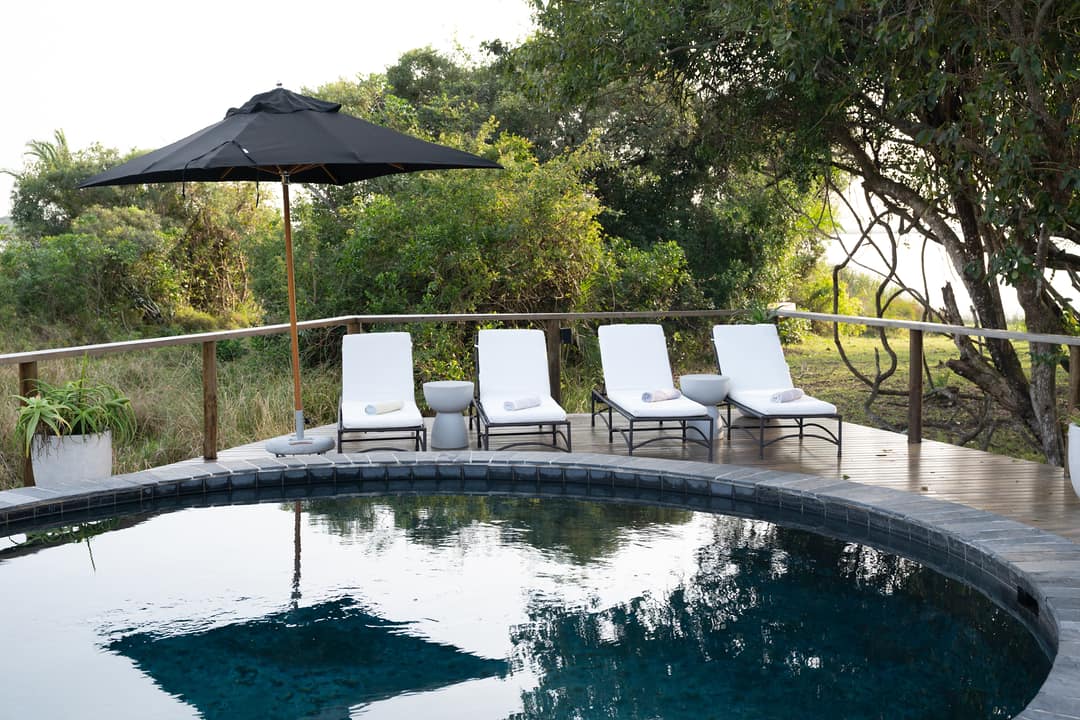 The round pool reflecting the trees, four loungers and a black umbrella on the deck