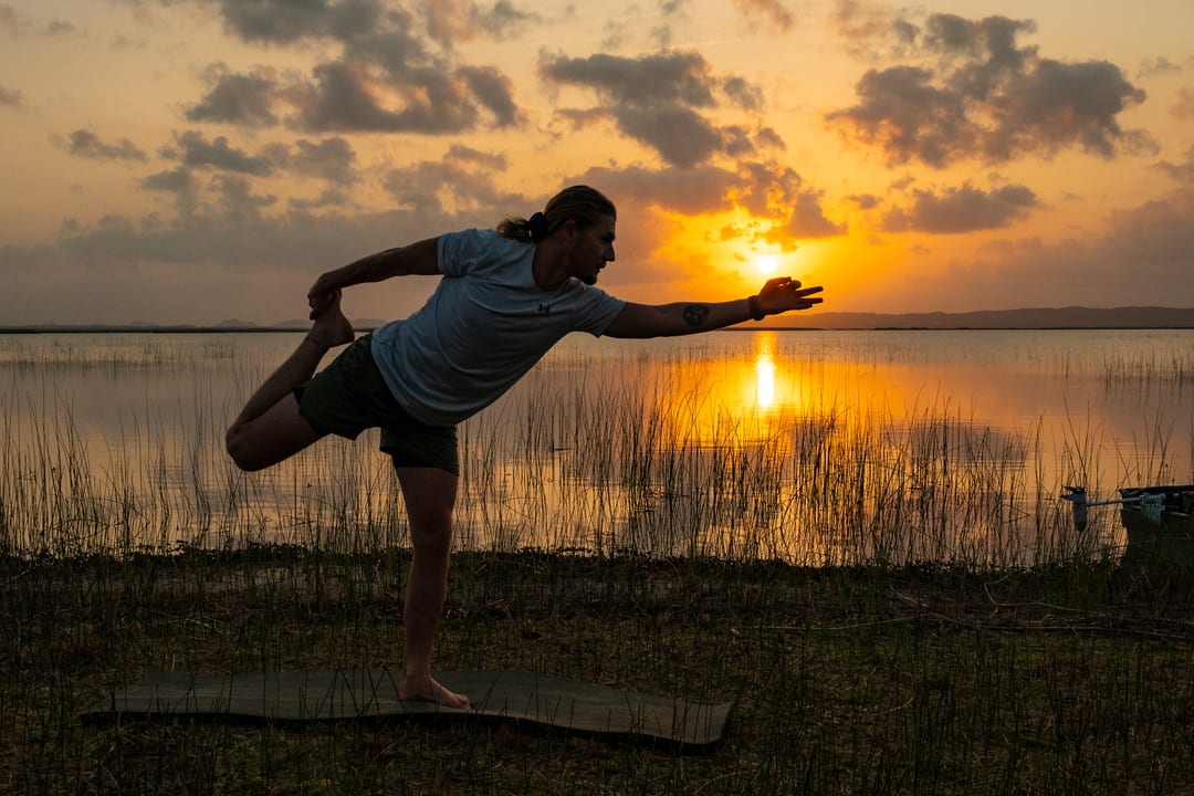 A guest in a yoga pose silhouetted against the rising sun over the lake shore