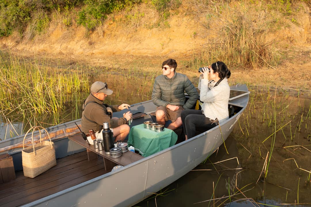 A guide sets out coffee in the boat while two guests look out over the reeds