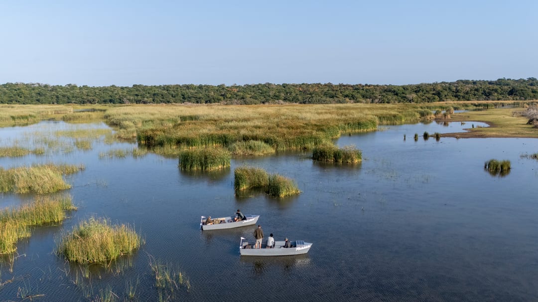 Aerial view of two solar-powered eco-boats among reed islands on the lake, coastal forest beyond.