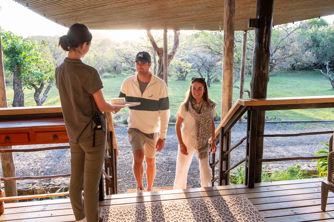 A member of the lodge team welcomes two arriving guests on the timber arrival deck