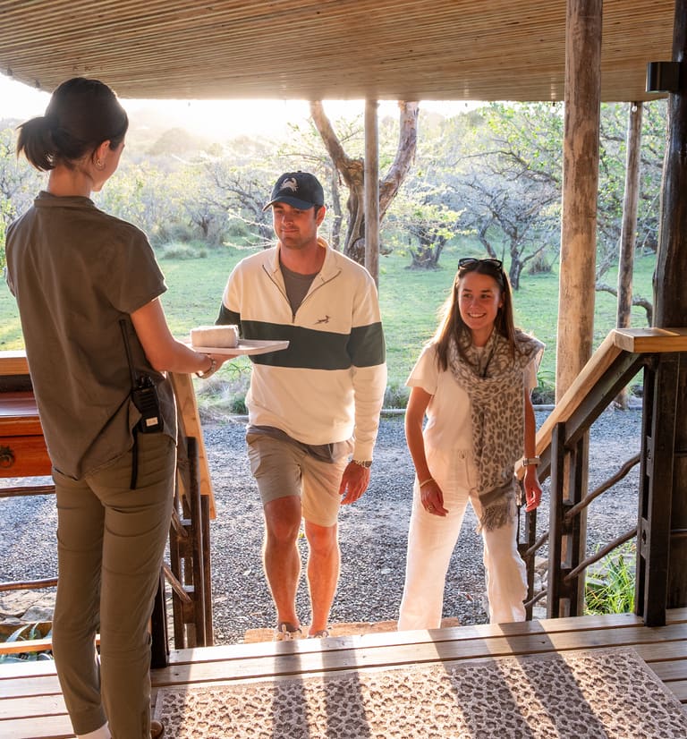 A lodge team member welcomes two guests up the entrance steps with a tray of rolled towels