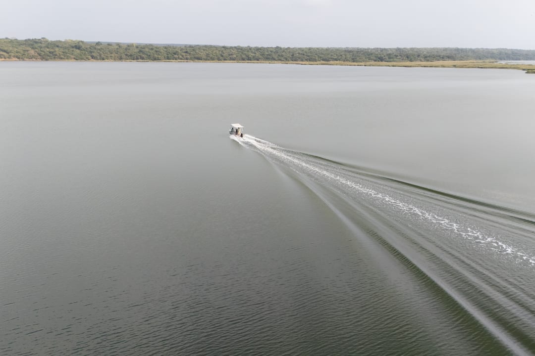 Seen from above, the lodge boat draws a long straight wake across the calm, open lake.