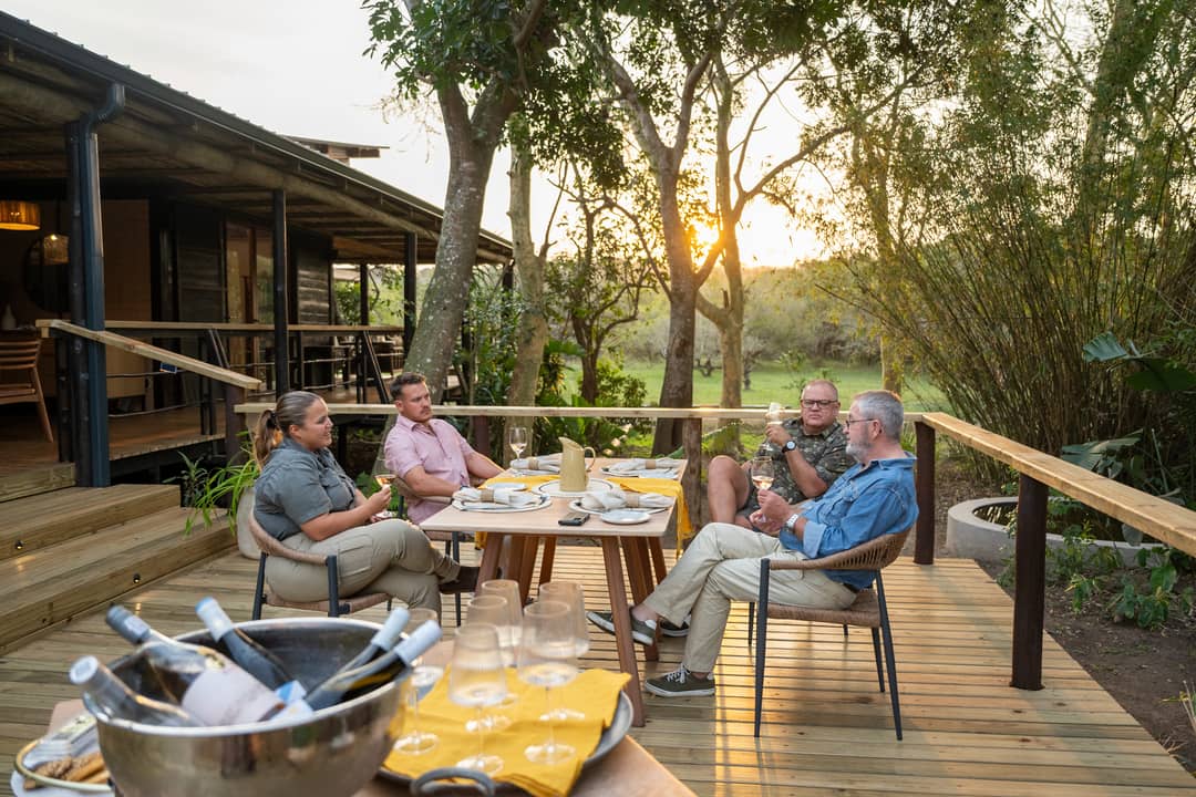 Four guests share wine at a table on the new deck as the sun sets through the trees