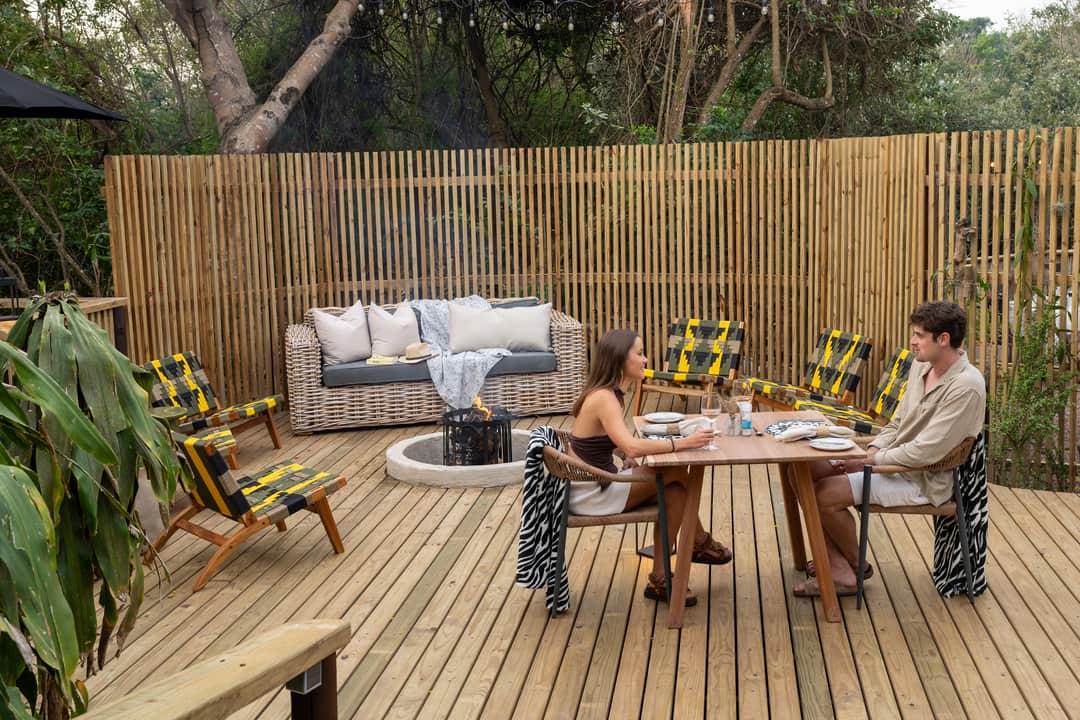 A couple share a table for two beside the fire pit on the deck boma by day.