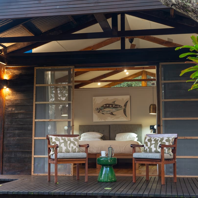 A Luxury Suite at dusk, its doors open to the lit bedroom and two chairs on the deck