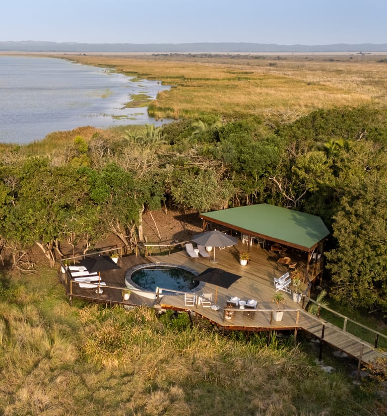 The pool deck and its green-roofed lounge pavilion from the air, set in coastal forest, with the reed beds and Lake St Lucia beyond.