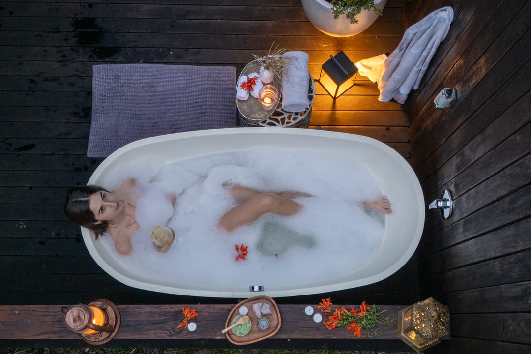Looking down on an outdoor bath at dusk, a guest in foam with a lantern and flowers