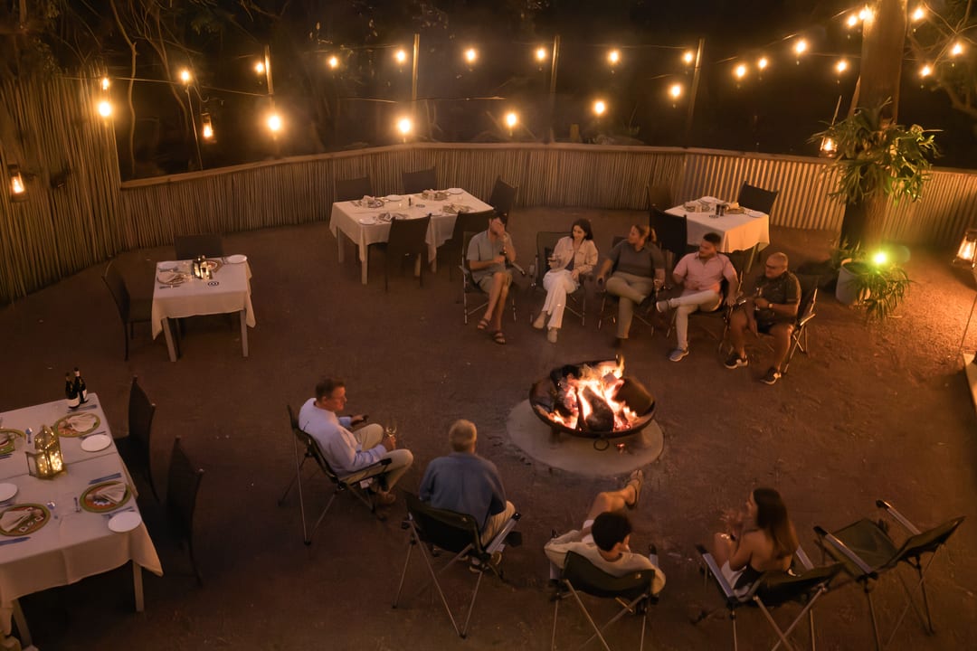 The main boma at night from above, tables laid under string lights and guests by the fire