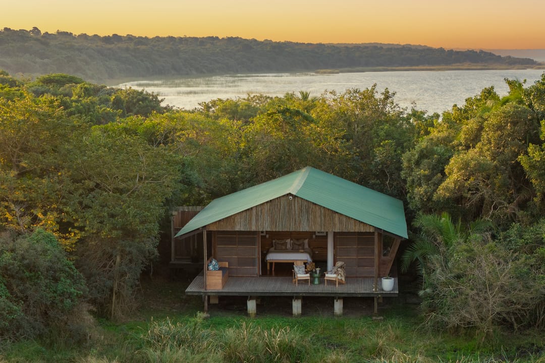 A green-roofed suite alone in coastal forest at sunset, the lake and far shore behind
